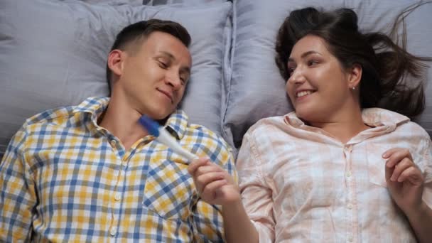 Jeune femme montre un homme un test de grossesse alors qu'il est couché au lit, rêverie, vue de dessus — Video