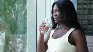 Pozitif Afro-Amerikalı kadın pencere kenarında su içiyor