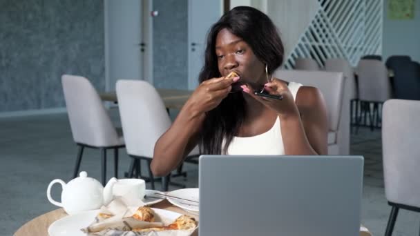 年轻的黑人妇女在咖啡店里通过电话吃比萨饼 — 图库视频影像