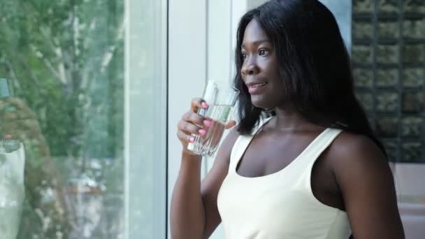 Mujer afro-americana positiva bebe agua por ventana — Vídeo de stock