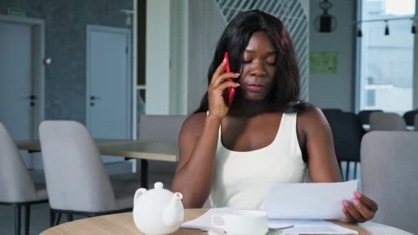 Afroamerikansk kvinna med papper pratar i telefon på caféet — Stockvideo