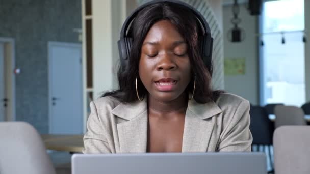 Mulher negra alegre com fones de ouvido fala em videocall — Vídeo de Stock