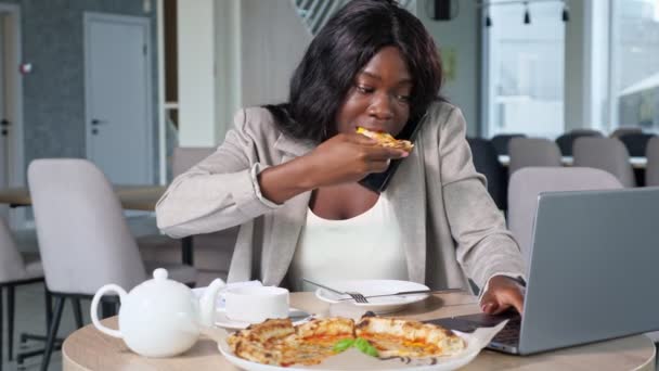 African-American woman talks on phone eating pizza in cafe — Stock Video