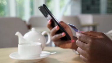 Siyahi bir kadın, kafede otururken telefonla ödeme yapıyor.