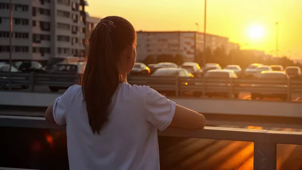 Jeune écolière avec queue de cheval regarde coucher de soleil sur le pont — Photo