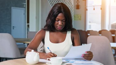 Afro-Amerikalı kadın kafedeki masada diyagramlarla çalışıyor.