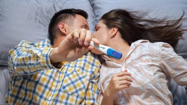 Kobieta pokazuje mężczyźnie test ciążowy leżący w łóżku, widok z góry, szczęście — Zdjęcie stockowe