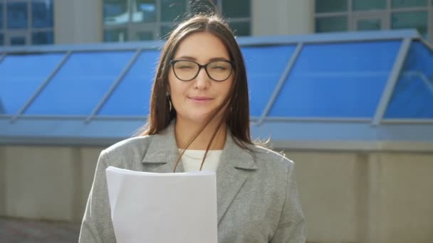 Ung kvinna i kostym och glasögon med papper leende på gatan — Stockvideo