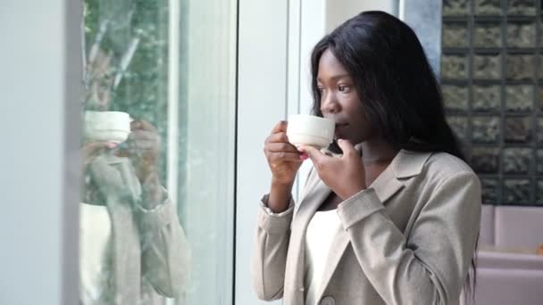 Mulher afro-americana bebe café perto da janela no escritório — Vídeo de Stock