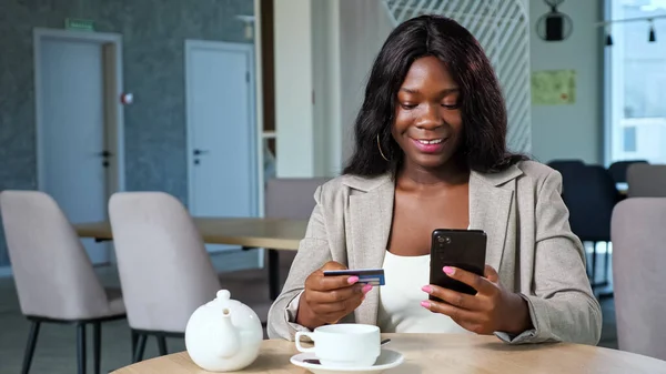 Black woman pays online with phone sitting at table in cafe