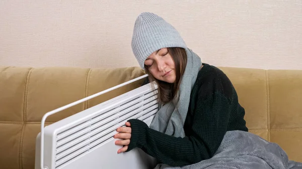 stock image Young woman hugs heater sitting on sofa in living room