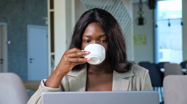 Afro-Amerikalı kadın kafede dizüstü bilgisayarla konuşuyor.