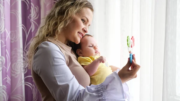 Heureuse jeune mère tient bébé fille dans les bras embrasser par la fenêtre — Photo