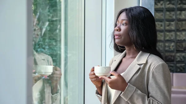 Mujer afroamericana bebe café cerca de la ventana en la oficina —  Fotos de Stock