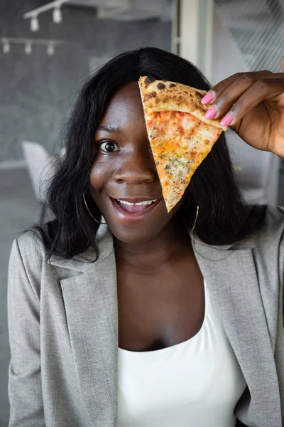 Mujer afroamericana en traje de negocios cubriendo los ojos con una rebanada de pizza —  Fotos de Stock