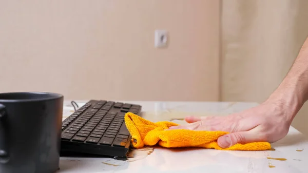 Mans hand wipes spilled coffee from table and keyboard — Stock Photo, Image