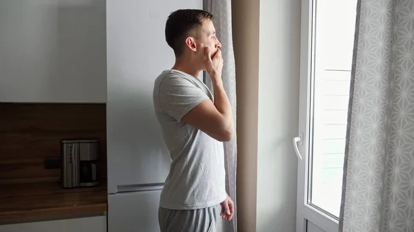 Un joven soñoliento se acerca bostezando a la ventana de la cocina — Foto de Stock