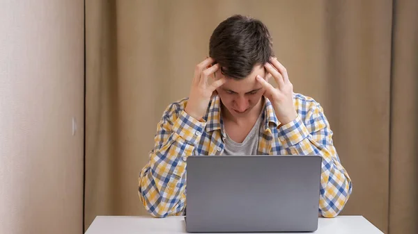 Joven hombre enojado escribiendo en el ordenador portátil en la mesa — Foto de Stock