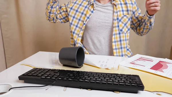 Homem irreconhecível trabalha com documentos e digita texto no teclado, joga café na mesa — Fotografia de Stock