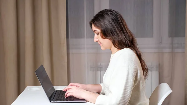 Concentrated brunette with long loose hair types on laptop