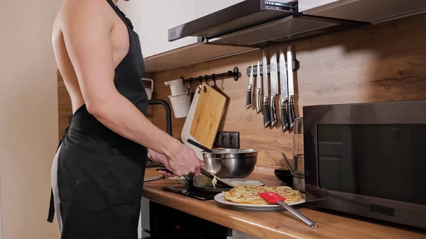 El hombre irreconocible con el torso desnudo y en el delantal negro prepara los crepes en la cocina — Foto de Stock