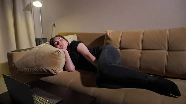 Молодая женщина лежит на коричневом диване с большими подушками и спит — стоковое фото