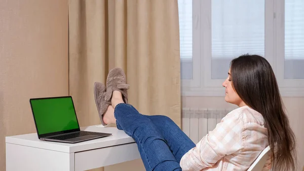 Jovem mulher jogando as pernas na mesa, olhando para um laptop com uma tela verde — Fotografia de Stock