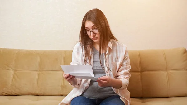 Woman opens envelope with bill and becomes nervous on couch — Stock Photo, Image