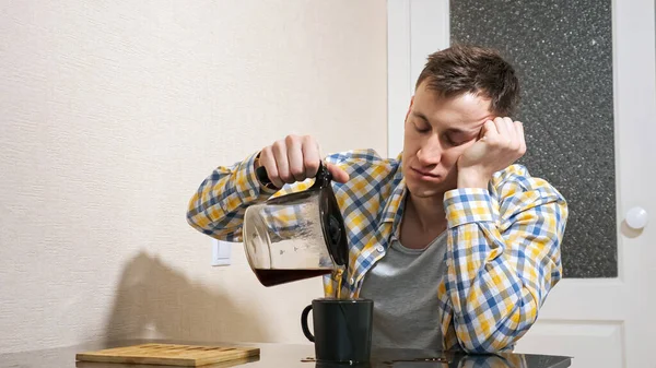 Сонный человек наливает кофе, сидя за столом на кухне — стоковое фото