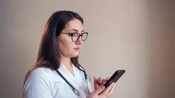 Doctor texts message on mobile phone near clinic beige wall