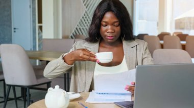 Siyahi iş kadını kafeteryada çay içip gazete okuyor.