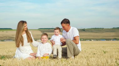 Küçük oğulları olan ebeveynler tarlada oturup gülümsüyor.