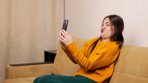 Joyful woman blogger in sweater grimaces sitting on sofa — Stock Photo, Image