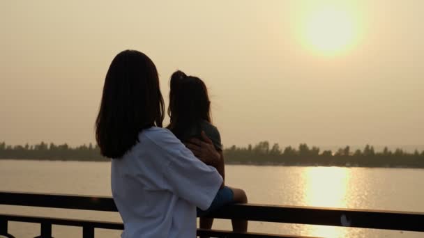 Mãe segura menina no corrimão à beira-mar ao pôr do sol — Vídeo de Stock