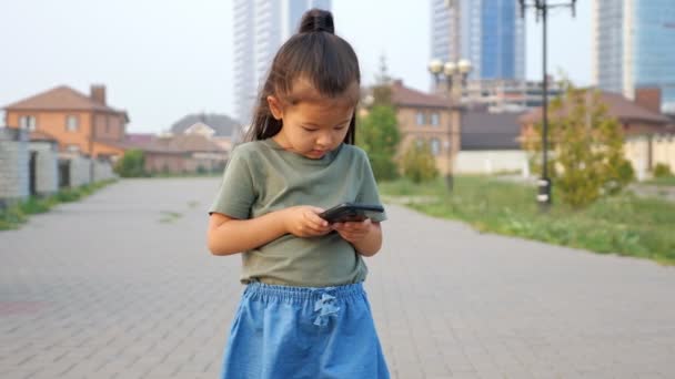 Poco asiático chica tipos mensaje en moderno teléfono móvil de pie al aire libre — Vídeos de Stock