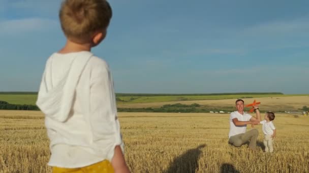 Mann fliegt rotes Spielzeugflugzeug in gemähtem Feld auf kleine Söhne zu — Stockvideo