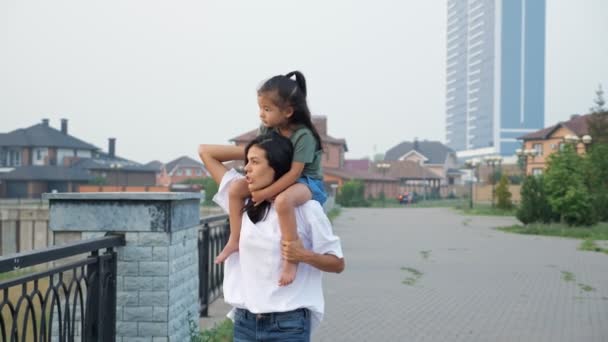 Η μαμά κουβαλάει την κόρη στους ώμους της περπατώντας στο ανάχωμα — Αρχείο Βίντεο