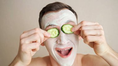 Yüzünde maske olan genç bir adam salatalık halkalarıyla oynar ve yüzünü buruşturur.