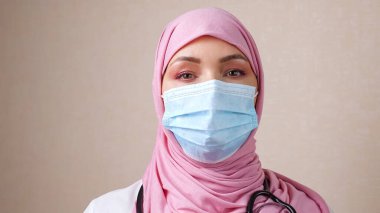 Boynunda fonendoskop ve yüzünde maske olan tesettürlü bir kadın doktor.