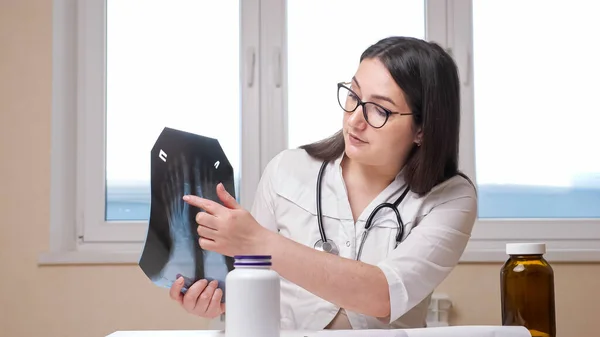 Mujer médico muestra imagen de rayos X de pies a cámara en el consultorio — Foto de Stock