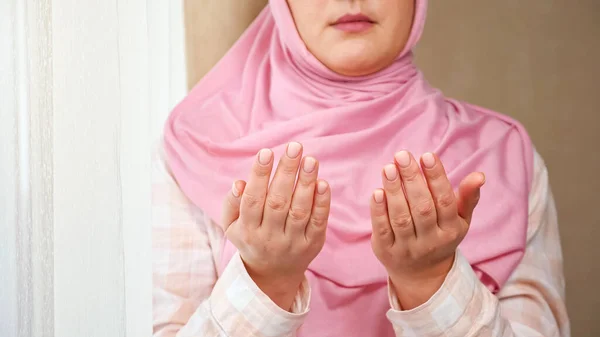 Неузнаваемая женщина в розовом хиджабе читает молитву, держа руки перед собой — стоковое фото