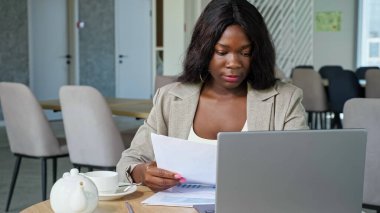 Siyahi iş kadını kafeteryada çay içip gazete okuyor.