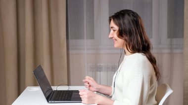 Beyaz kazaklı ve siyah kulaklıklı genç bir kadın sohbet ediyor.