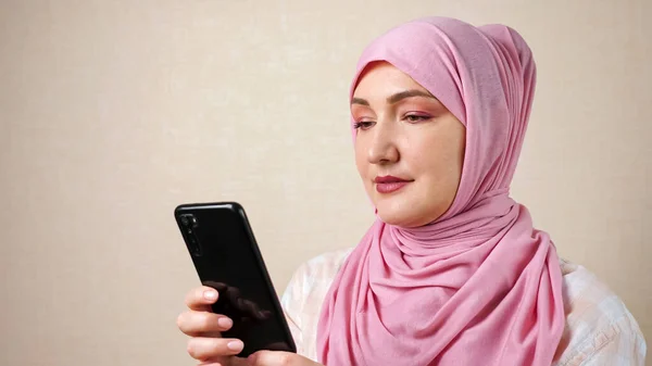 Mujer musulmana en una bufanda con un teléfono en las manos está escribiendo texto — Foto de Stock