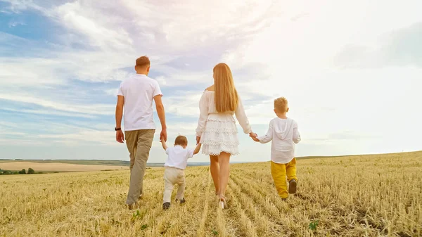 Família com crianças caminha unindo as mãos no campo de trigo cortado — Fotografia de Stock