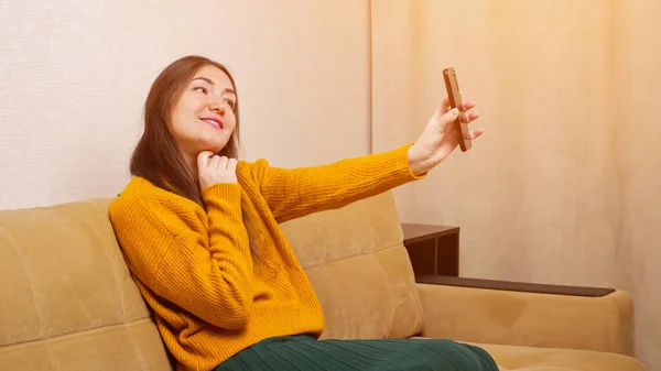 Young brunette holds smartphone and poses into front camera — Stock Photo, Image