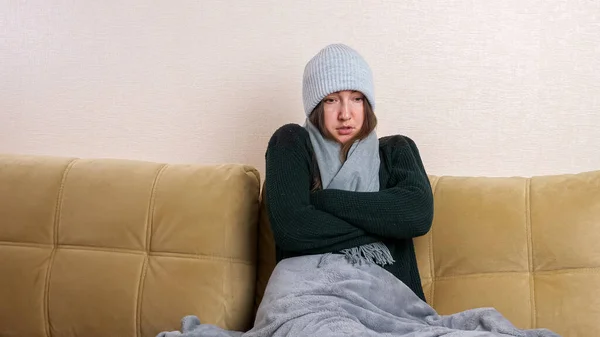 Mujer con cuadros pone en la bufanda sentado en el sofá en la habitación fría — Foto de Stock