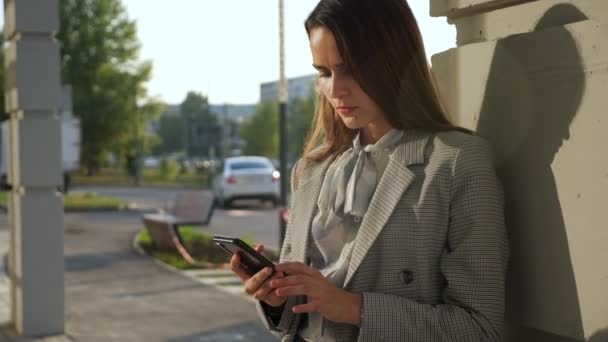 Νεαρή γυναίκα με ένα επαγγελματικό κοστούμι με ένα τηλέφωνο στέκεται στο δρόμο — Αρχείο Βίντεο