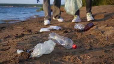 Eldivenli iki tanınmayan insan nehir kıyısında plastik çöp topluyor.