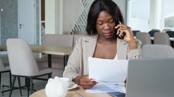 Femme afro-américaine avec des journaux parle au téléphone dans un café — Video